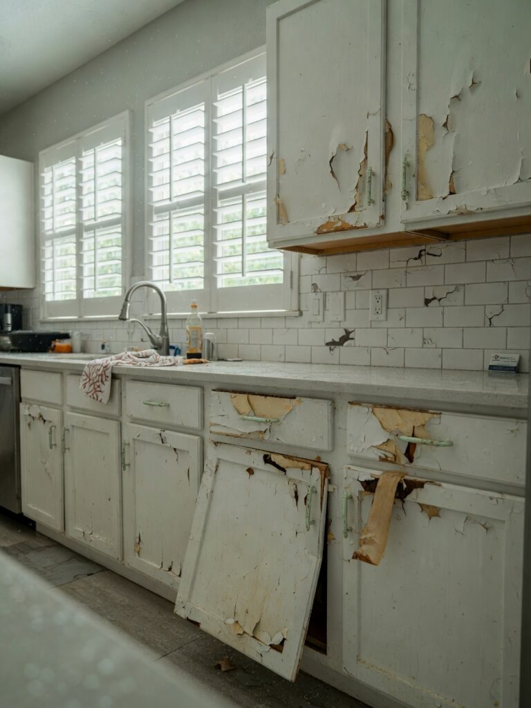 Ultra-realistic 8K photo of a modern South Fort Myers kitchen with damaged peeling cabinets due to salt air corrosion, natural daylight coming through windows, showing swollen cabinet doors, professional photography, sharp detail